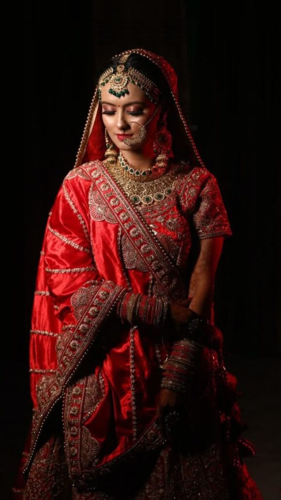 Indian bride in a red and gold embroidered lehenga, adorned with traditional jewelry, captured beautifully by Pixel Chaser.